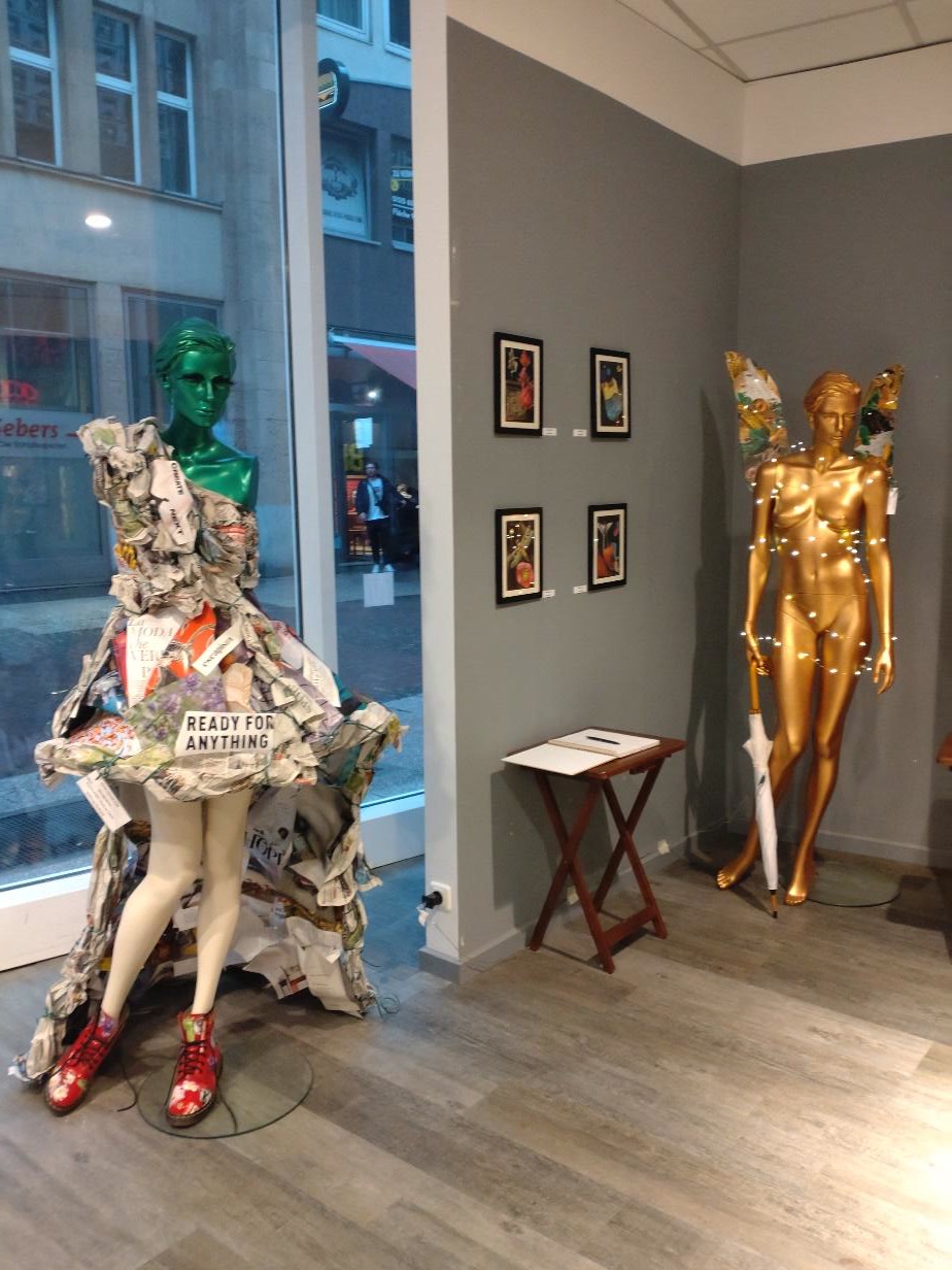 A collage dress on a mannequin beside a gold mannequin with collage wings in a Hannover exhibition.